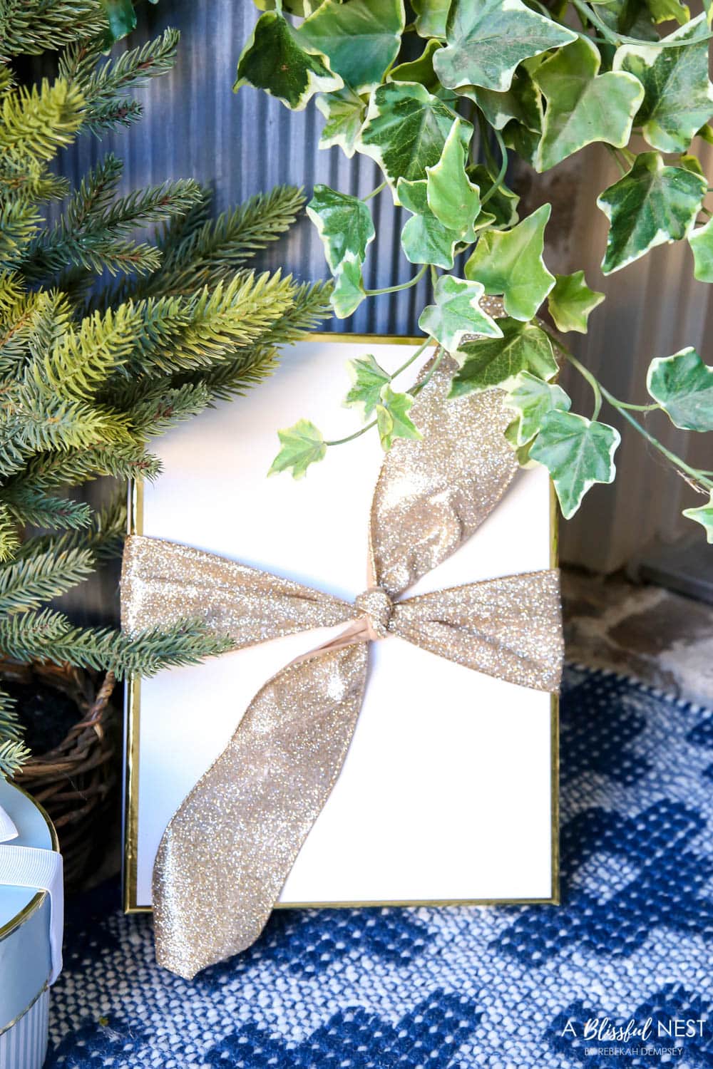 White gift box with gold glitter ribbon next to a planter on a front porch.