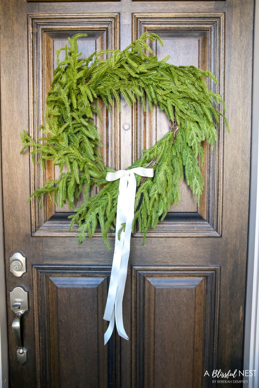 Juniper wreath with white satin ribbon tied in a bow on a front door.