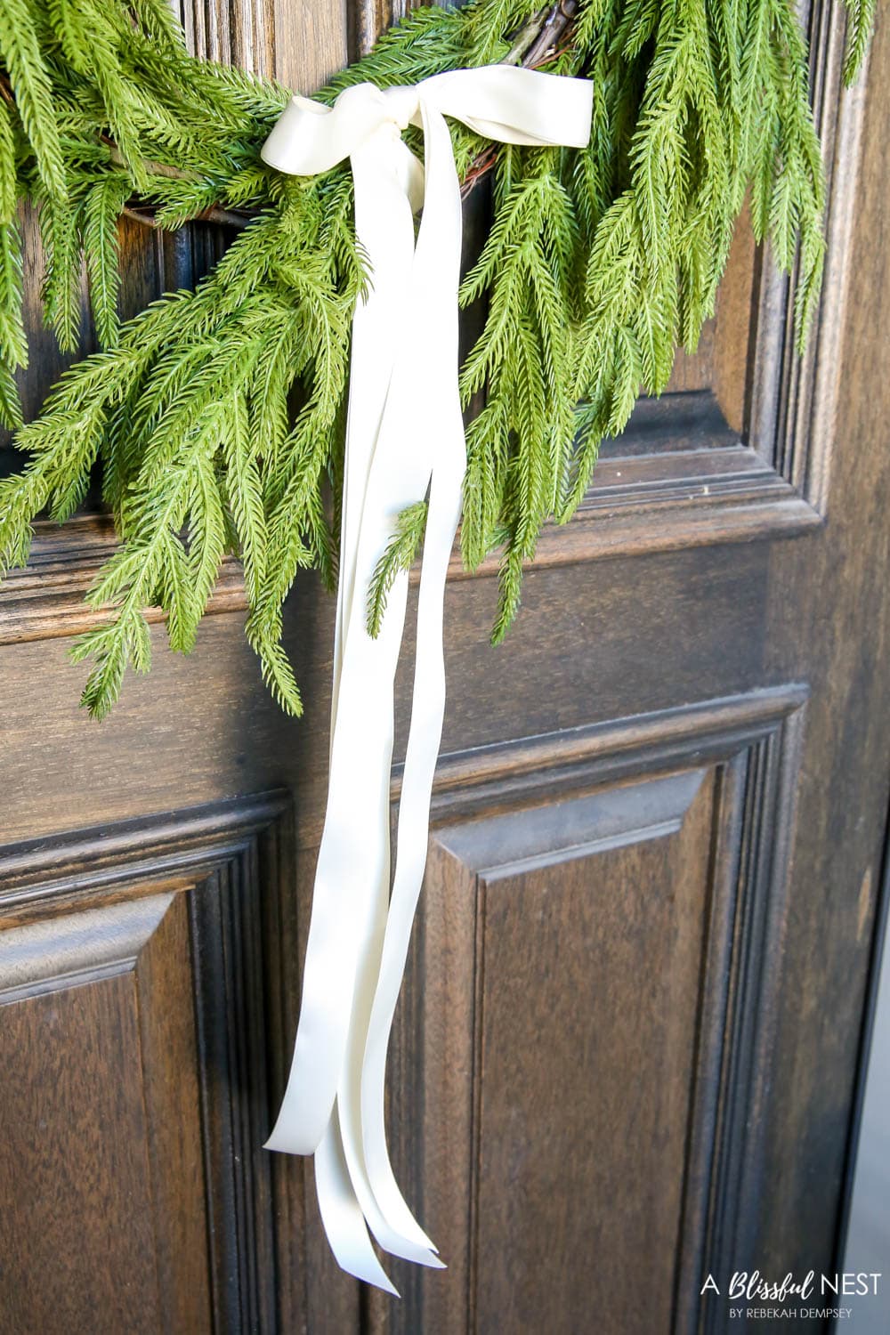 Juniper wreath with white satin ribbon tied in a bow on a front door.