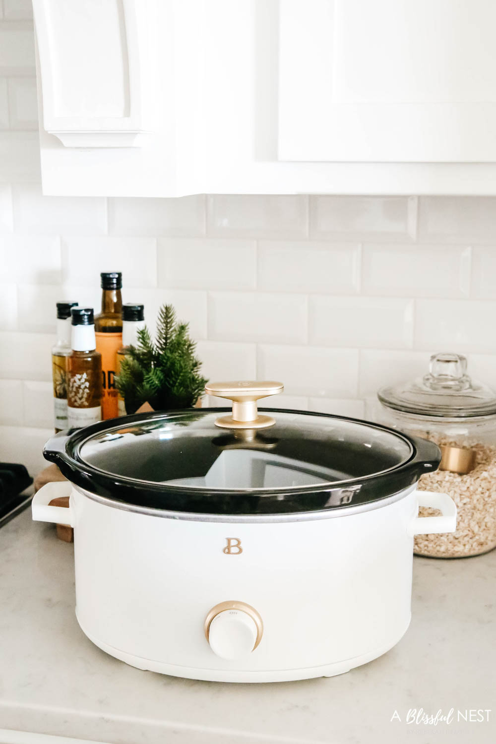 A modern white crockpot sitting on a counter near baking jars.