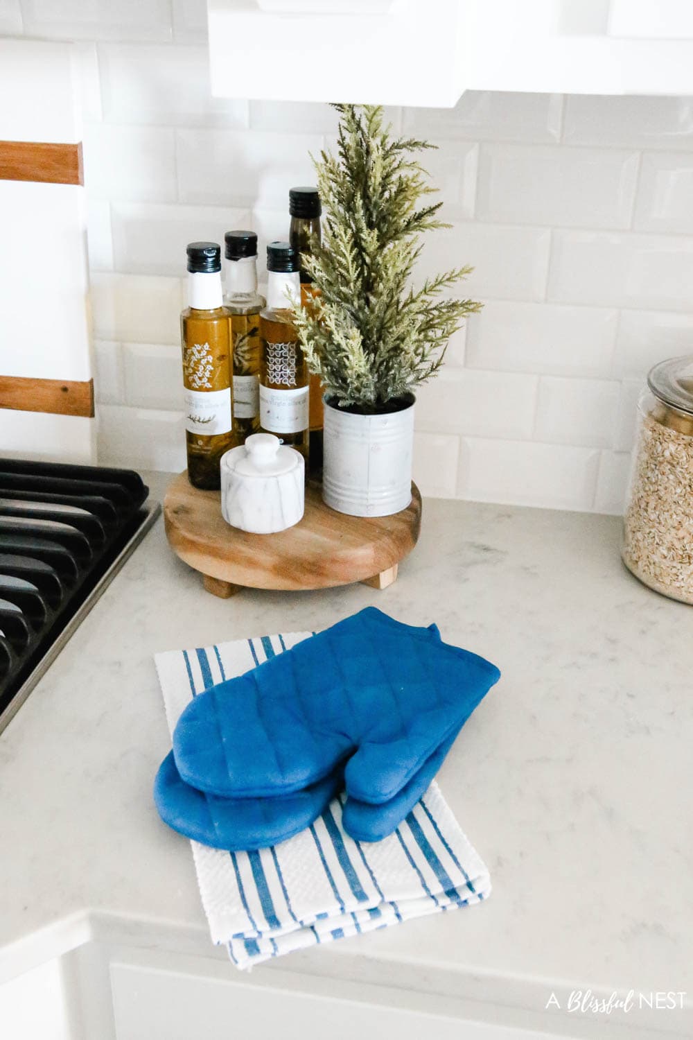 Navy blue pot holders sitting on blue and white striped dish towels on a counter next to a cooking range. 