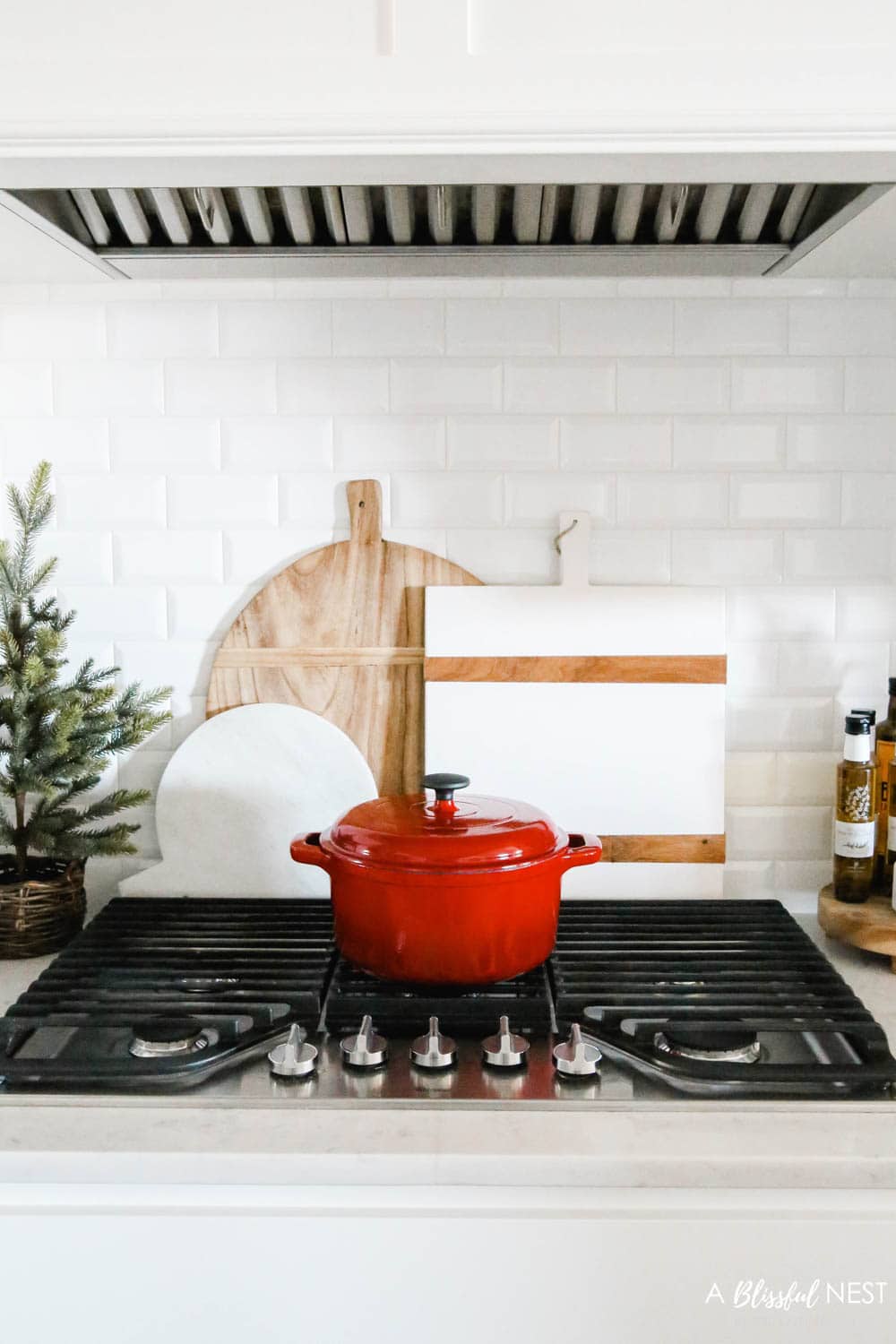 red cast iron cooking pot sitting on a cooktop with a cluster of 3 cutting boards behind it.