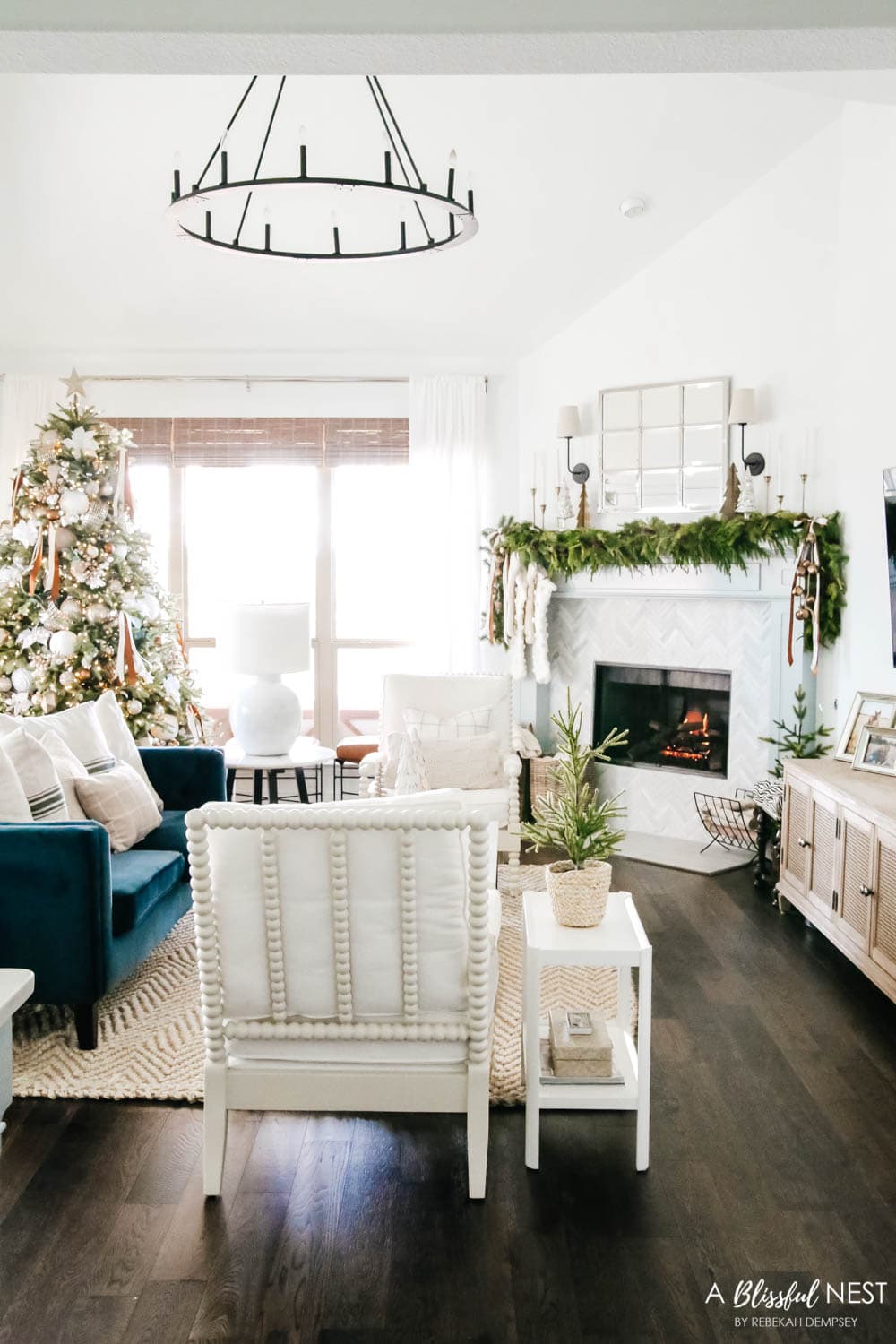 Navy blue velvet sofa facing a fireplace mantle. Green holiday garland with a mirror above