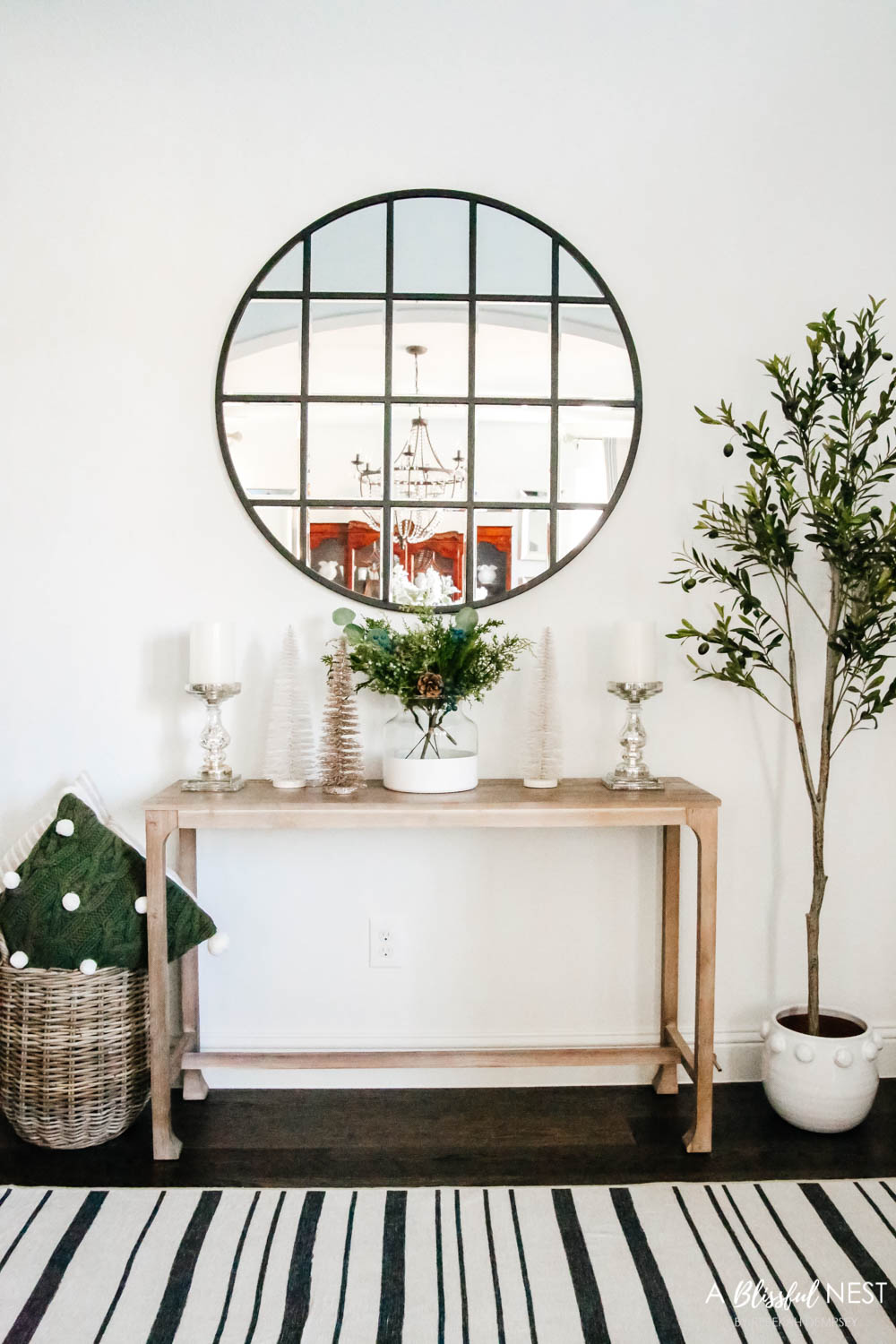 An entryway decorated for Christmas with garland up the staircase and neutral and green holiday decor. Christmas entryway, holiday entryway