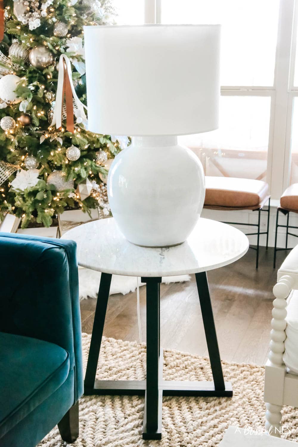 Marble topped side table with round white table lamp in front of a Christmas tree