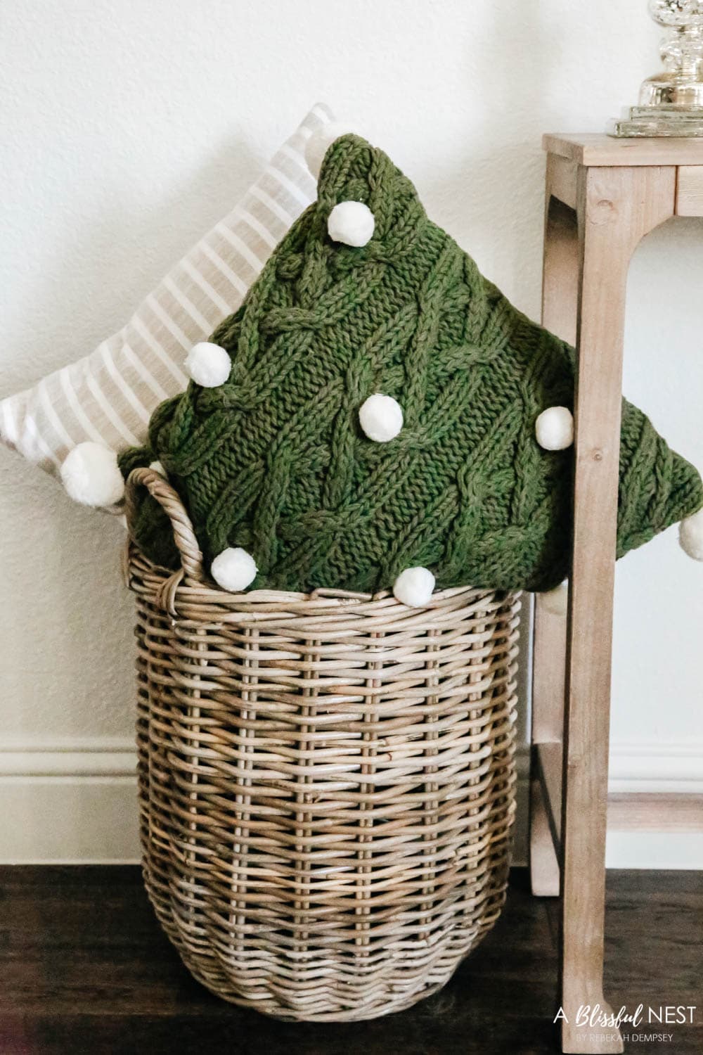 Green pillow with white pom pom trim and a beige striped pillow in a basket next to the entry table.