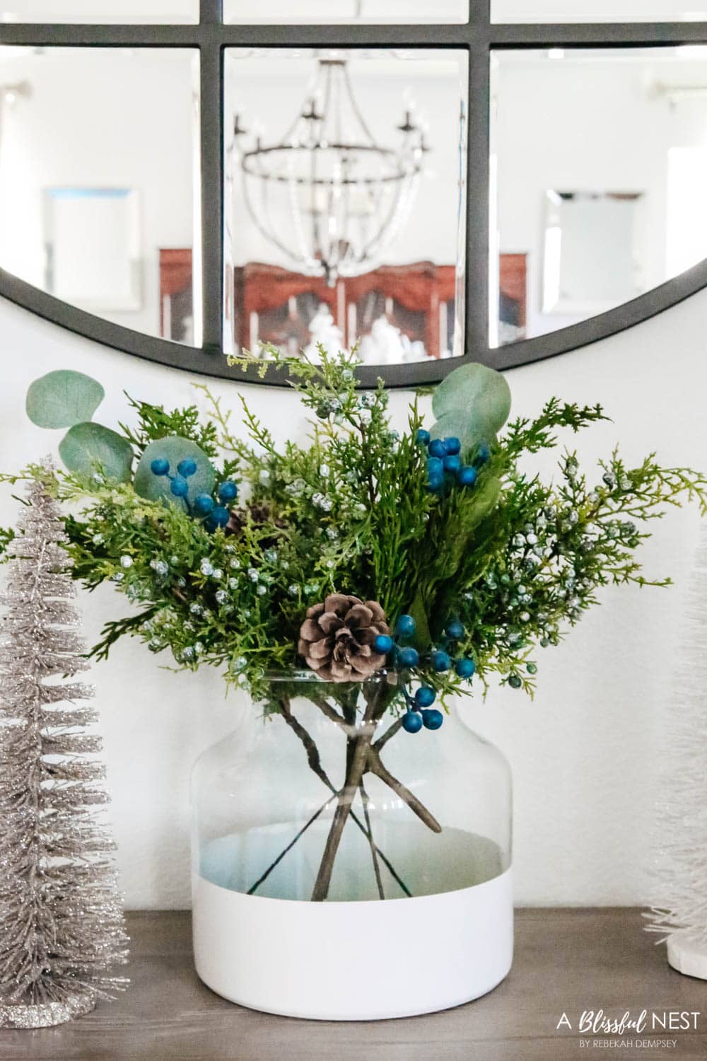 Juniper stems in a white vase on a entry table.