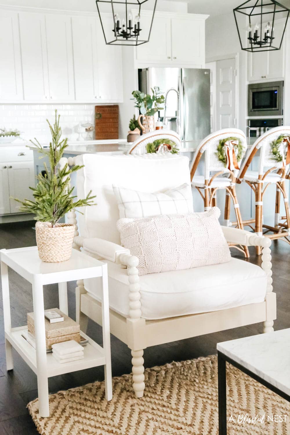 White spindle chair with neutral pillows and white side table with mini tree in basket on top