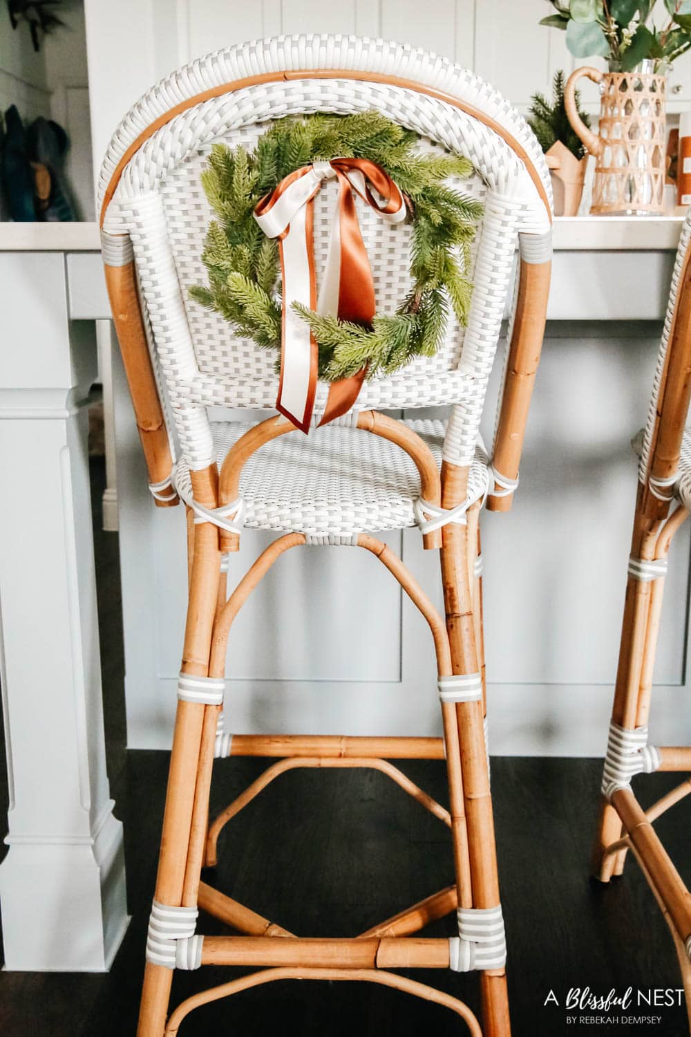 Grey and white rattan barstools in a white kitchen with mini wreaths tied on the back of them.