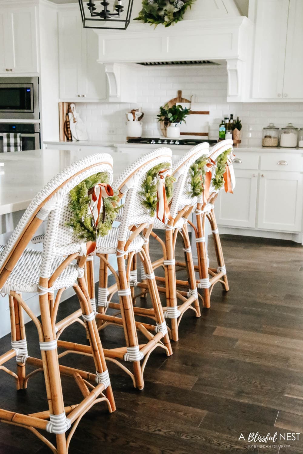 Grey and white rattan barstools in a white kitchen with mini wreaths tied on the back of them.