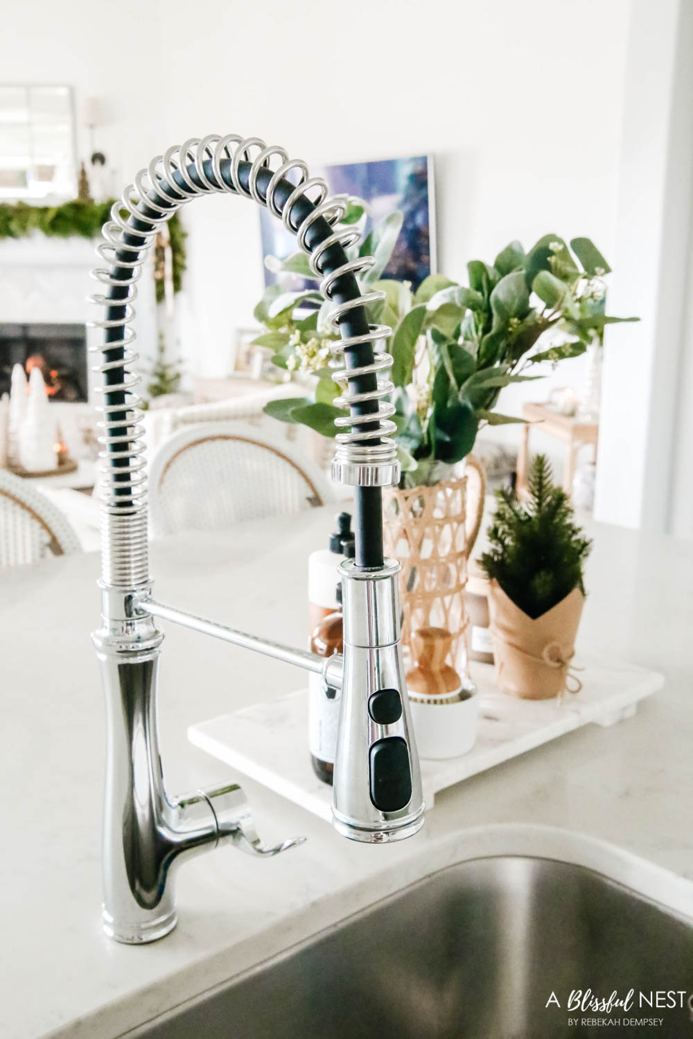 Kitchen faucet with a marble tray with soap and holiday greenery in a vase.