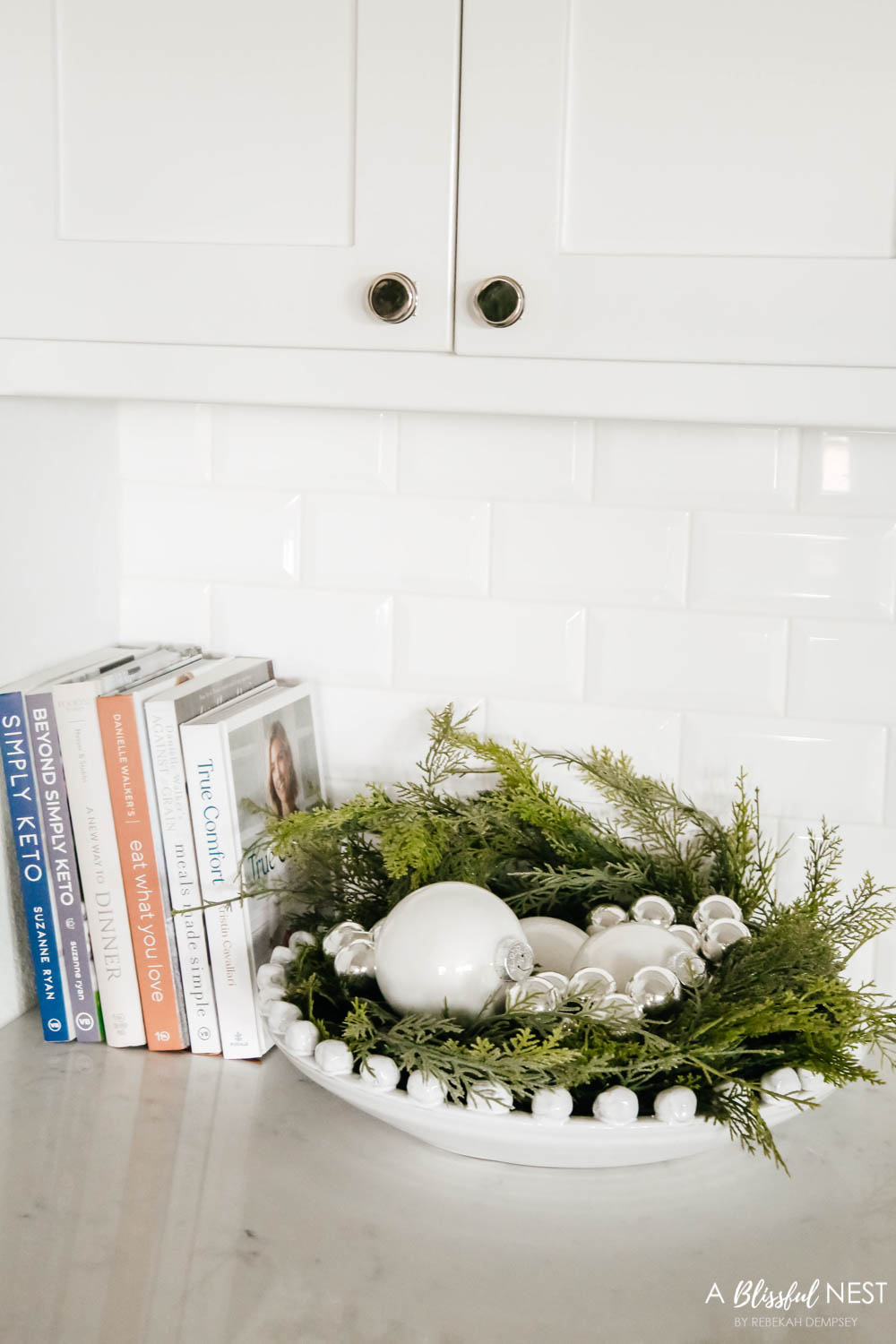 White bowl with greenery and ornaments sitting next to cookbooks in a white kitchen