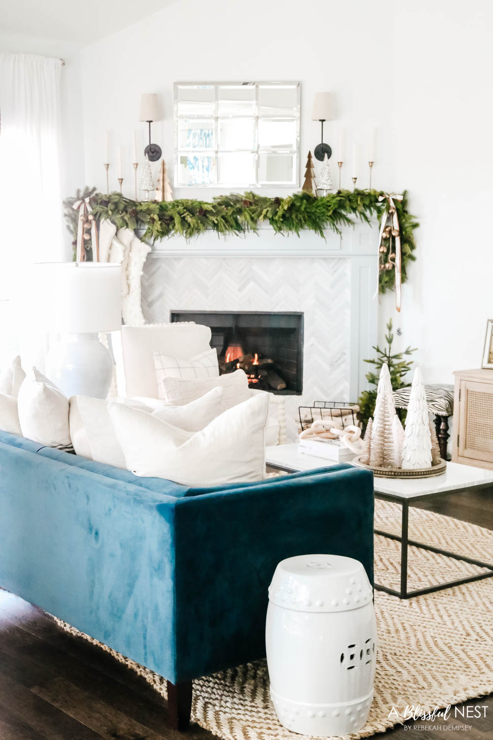 Navy blue velvet sofa facing a fireplace mantle. Green holiday garland with a mirror above