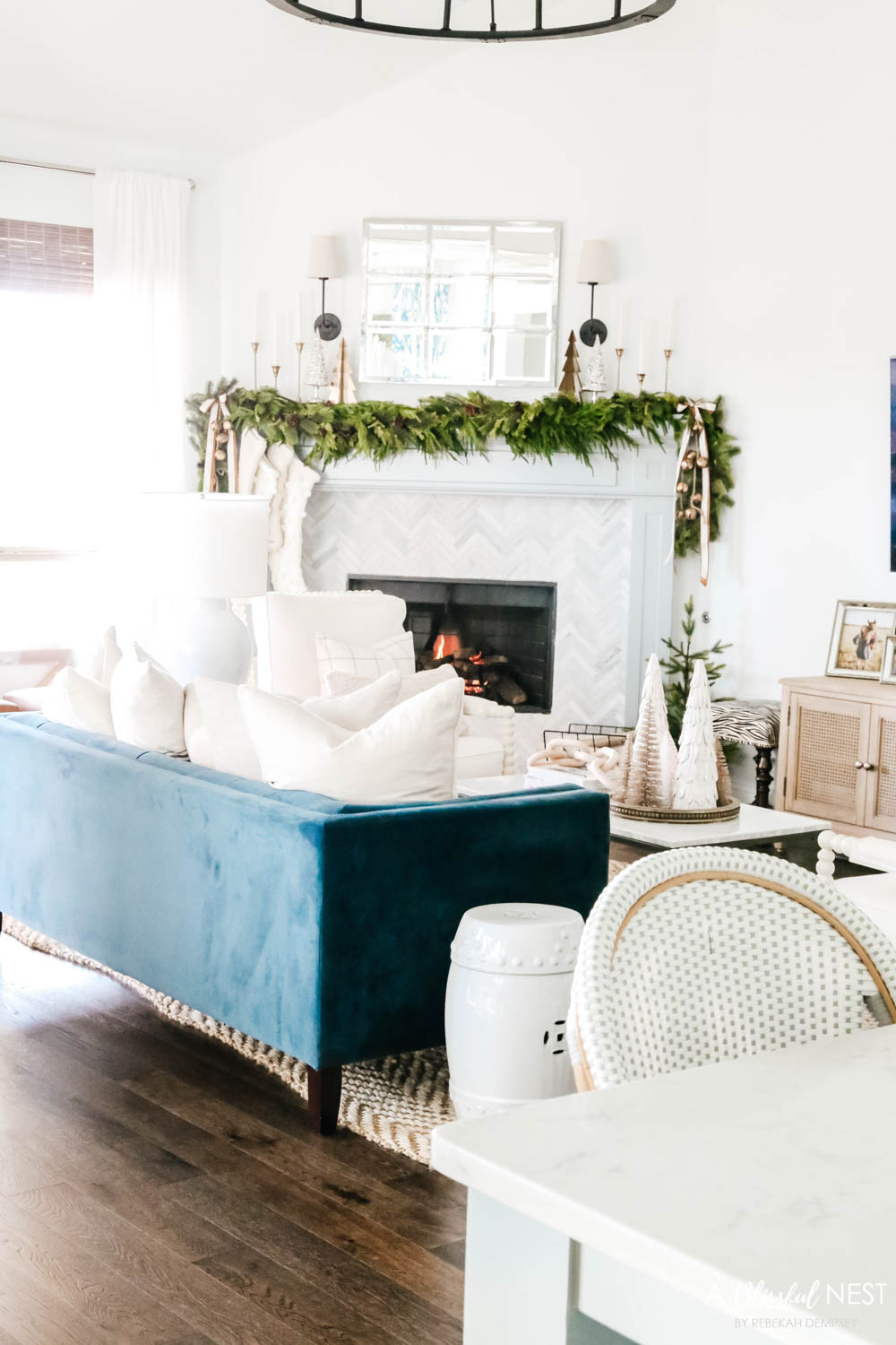 Navy blue velvet sofa facing a fireplace mantle. Green holiday garland with a mirror above