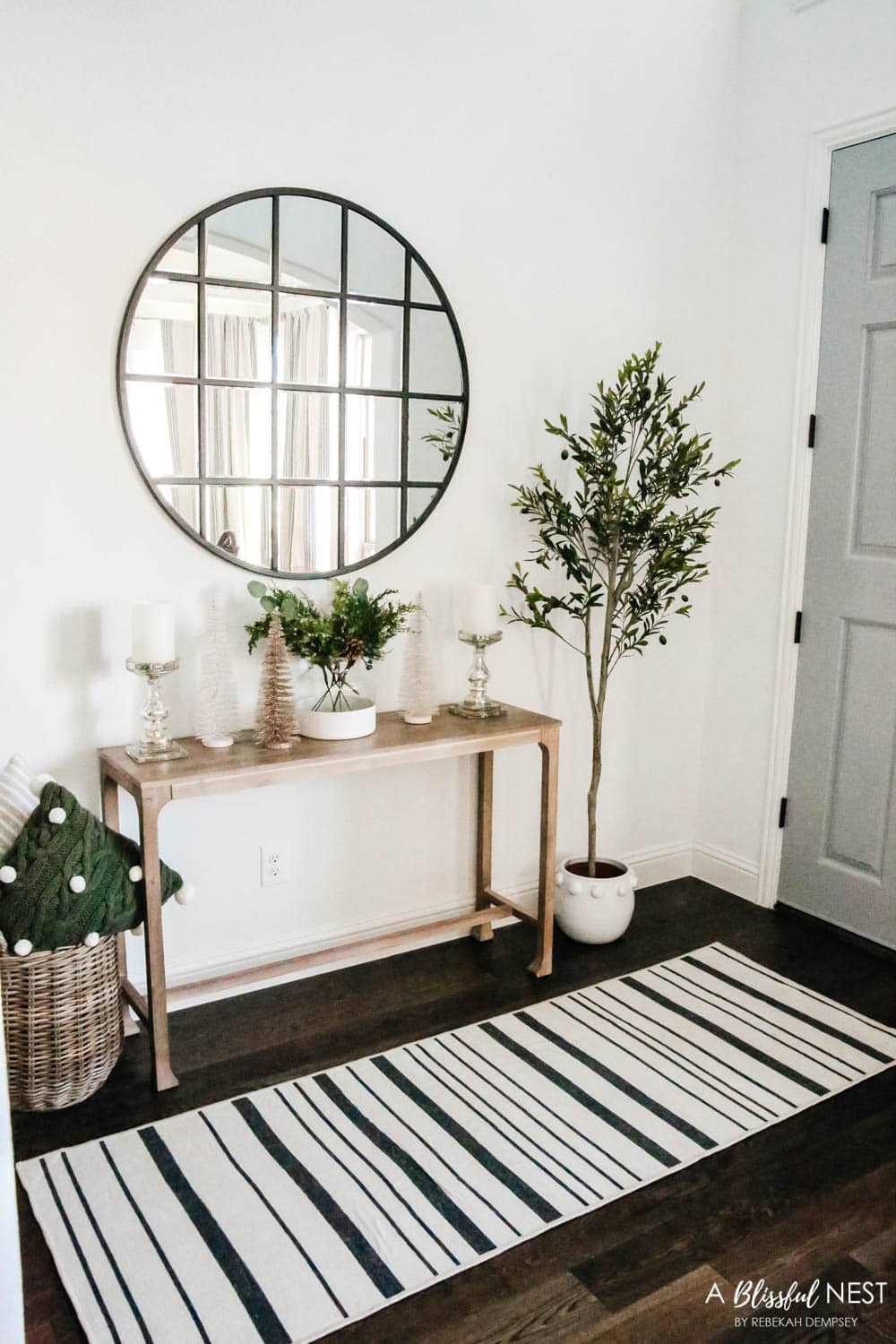 An entryway decorated for Christmas with garland up the staircase and neutral and green holiday decor. Christmas entryway, holiday entryway