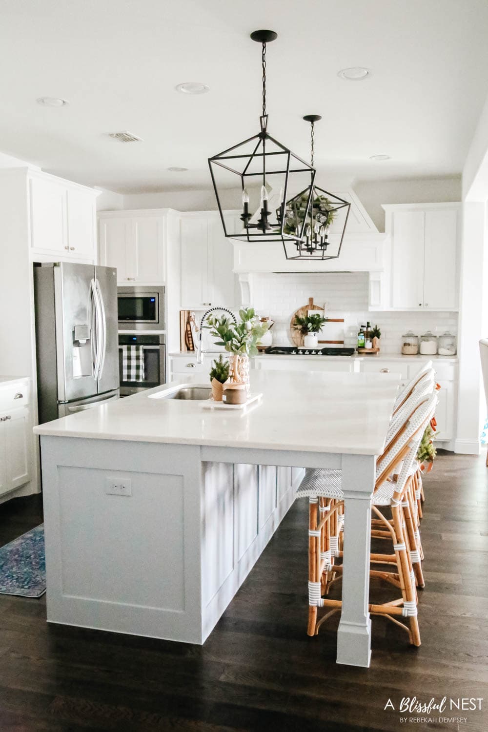 Grey and white rattan barstools in a white kitchen with mini wreaths tied on the back of them.