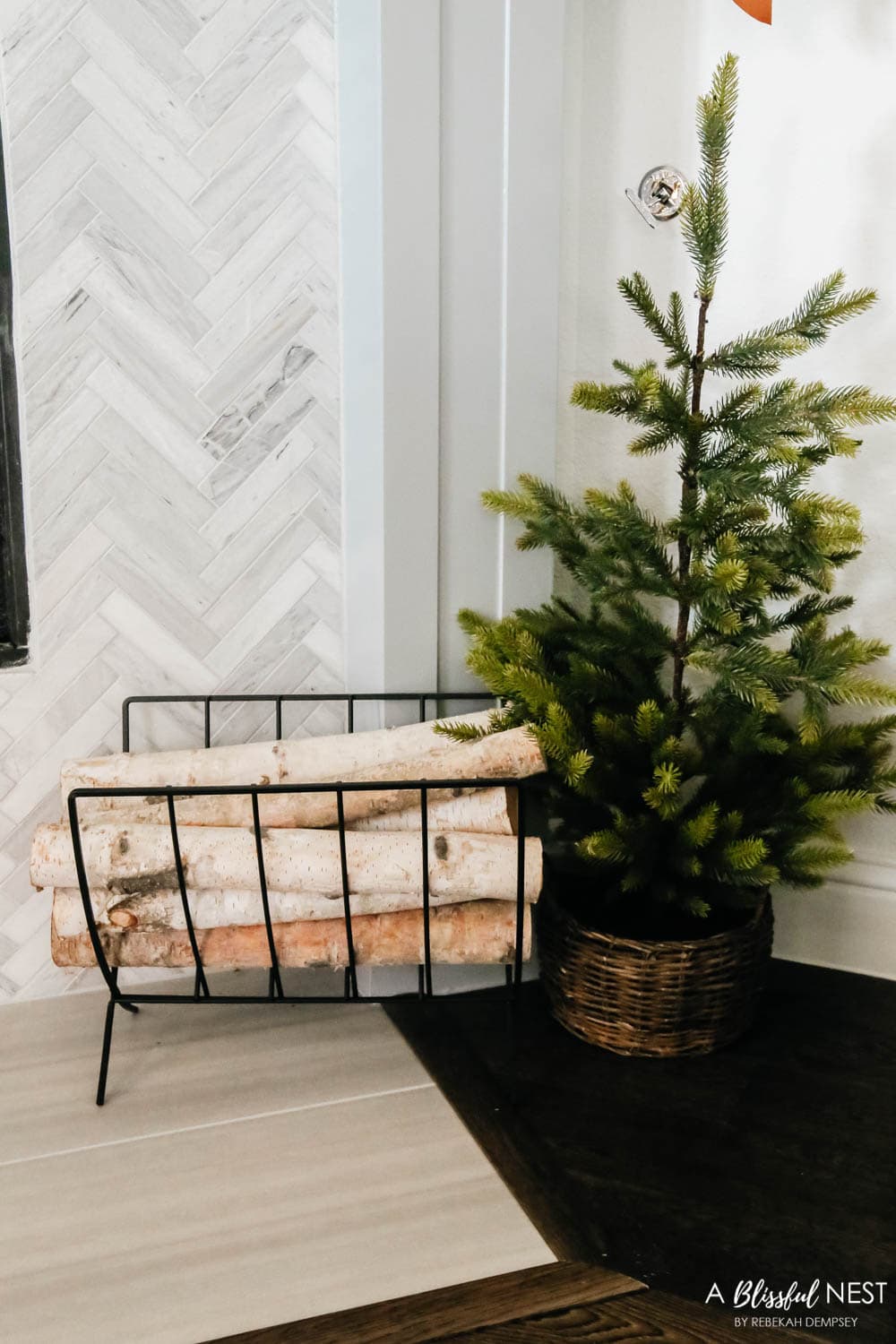 Birch logs in a black metal log holder and small Christmas trees in baskets.