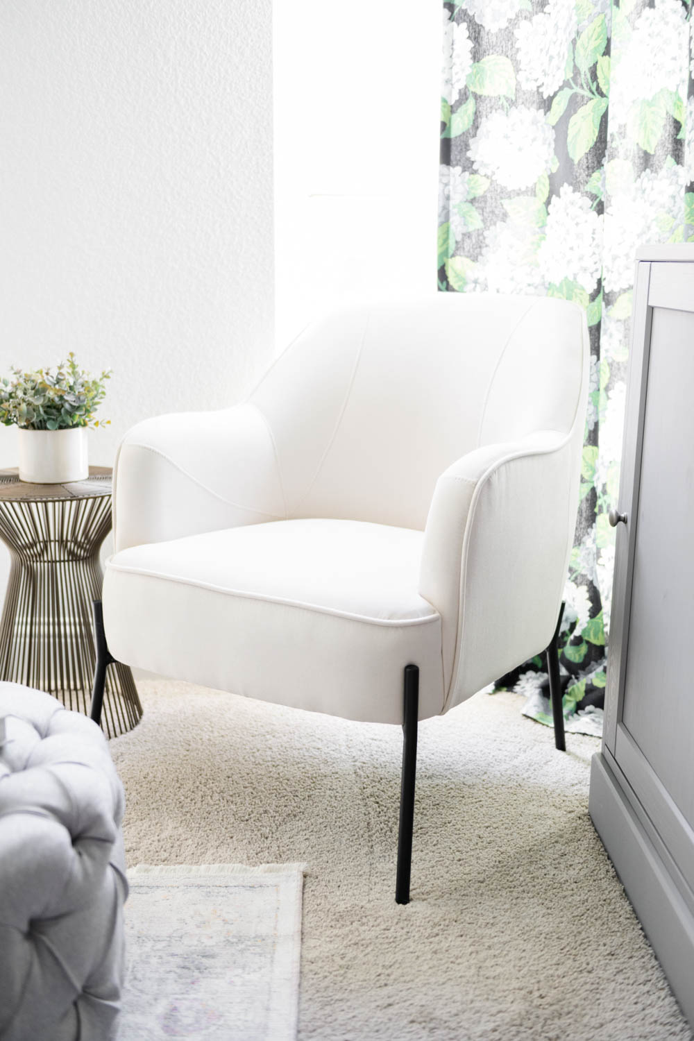 Modern white chair with black iron legs in front of a window.
