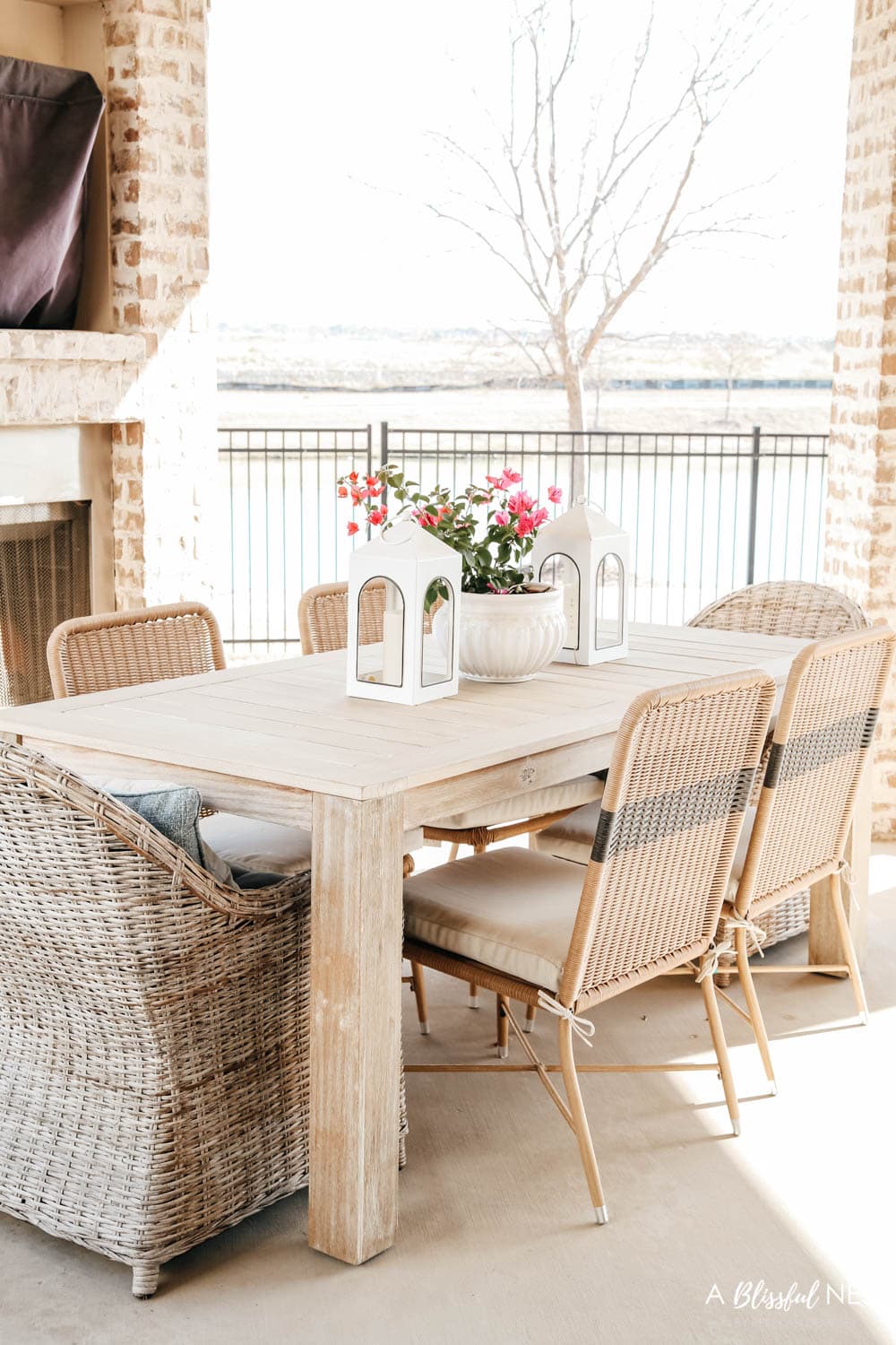 Outdoor table with weave chairs and white lanterns with a pink bougainvillea plant