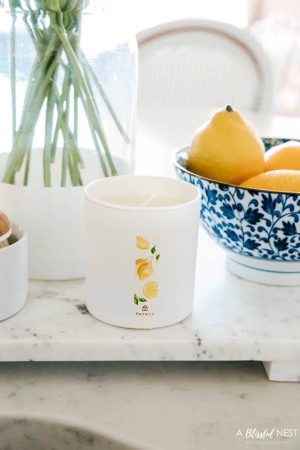 Lemon scent candle on a marble tray next to a blue and white bowl filled with lemons.