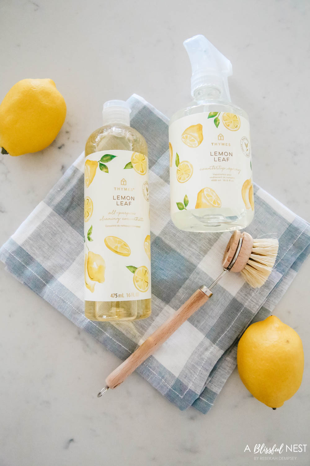 Lemon scented cleaners for your kitchen laying on a blue and white dish towel with a dish scrub brush