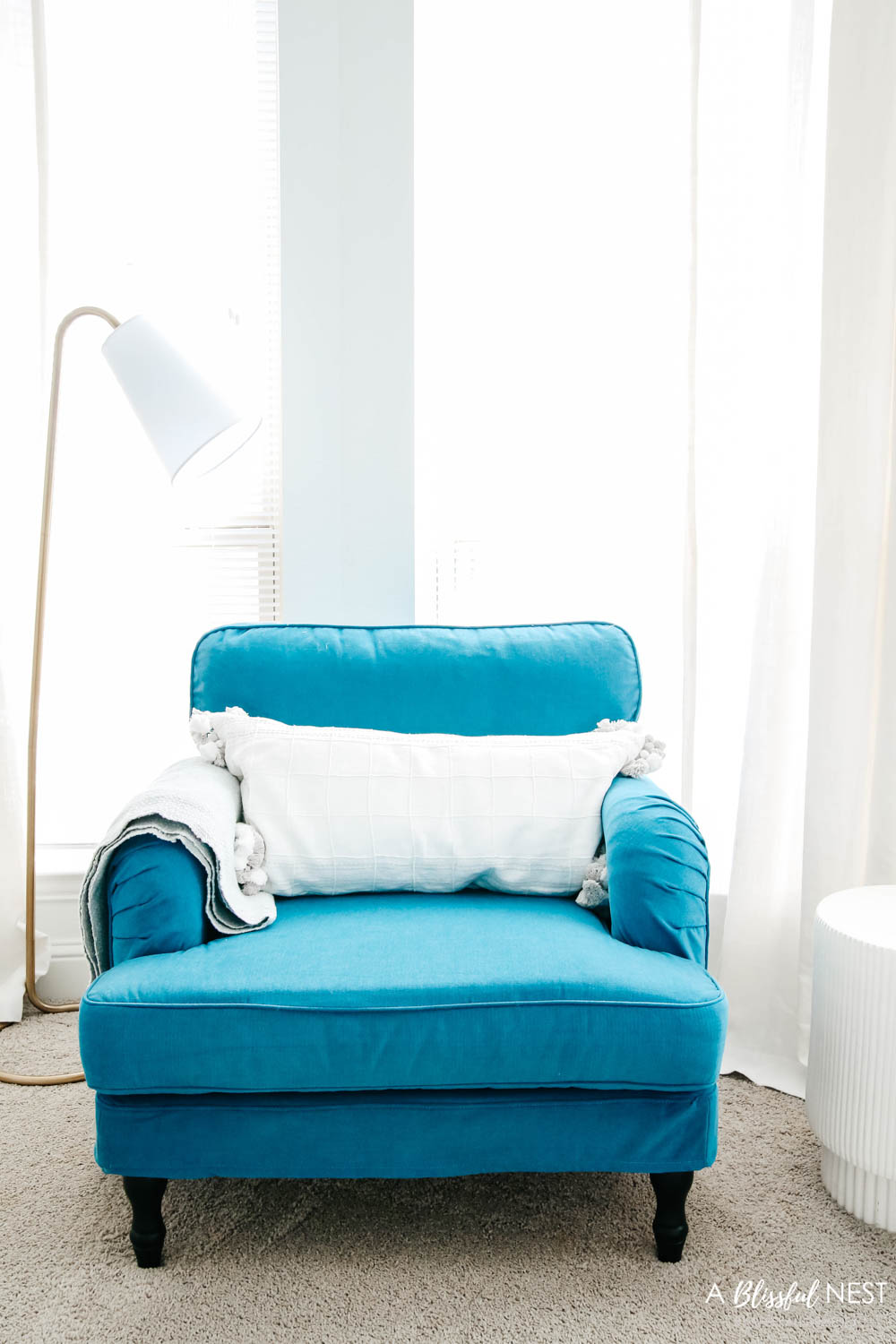 Cozy blue chair with throw blanket and gold floor lamp next to it.