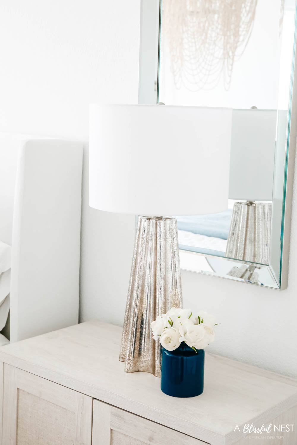 Mercury glass table lamp with navy blue vase with flowers sitting on a nightstand