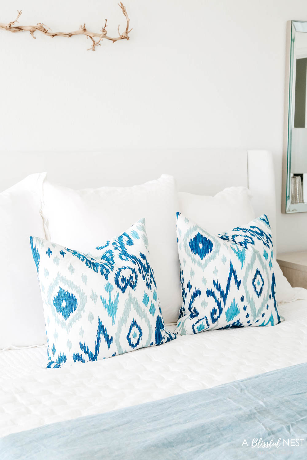 Blue and white ikat patterned pillows on a bed with white bedding