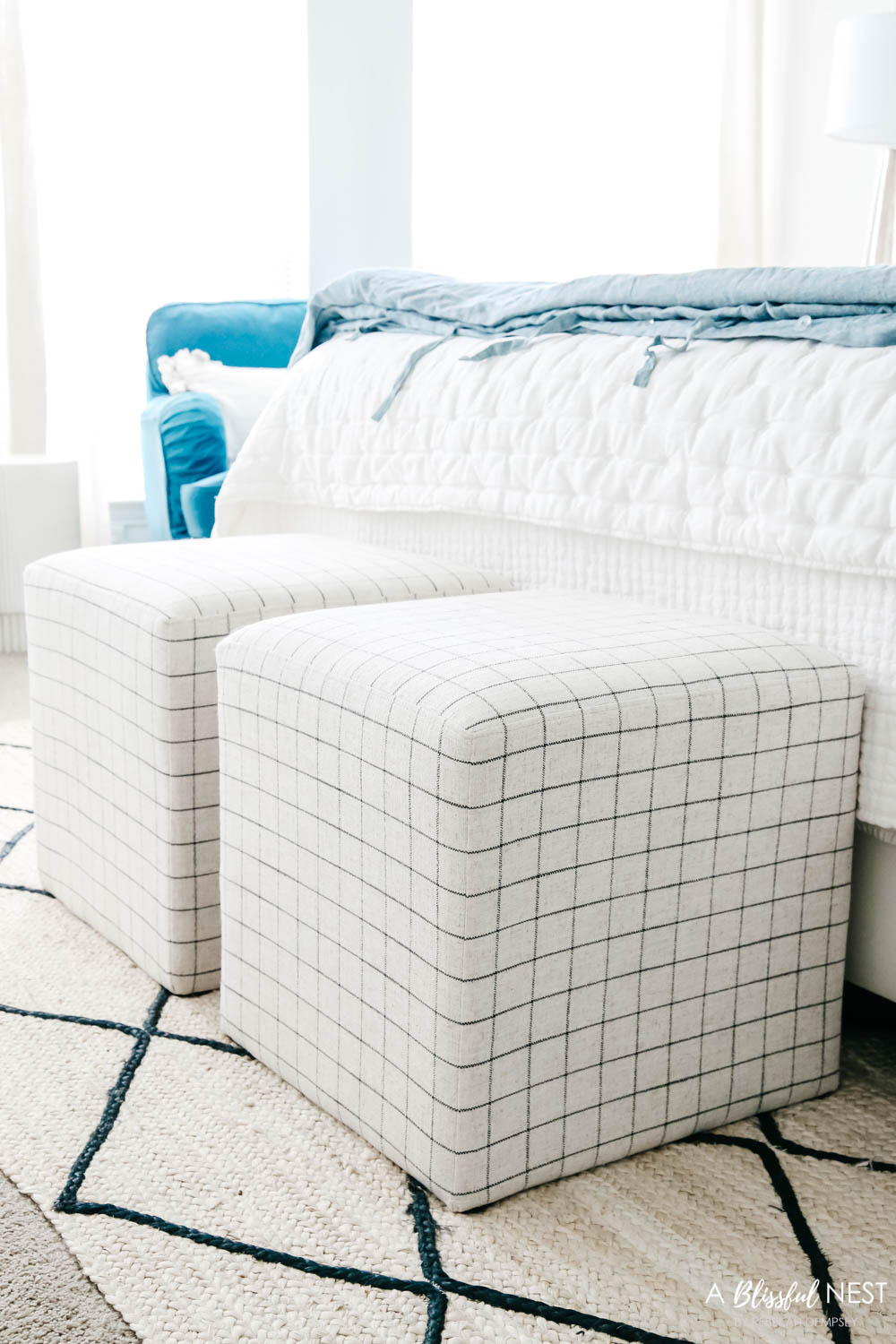 Cream and black check patterned square ottomans placed at the end of the bed