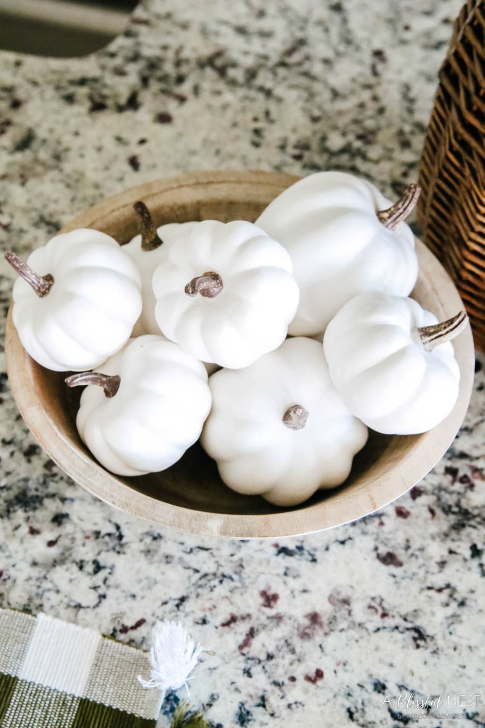 small wood bowl filled with mini white pumpkins on a kitchen counter.