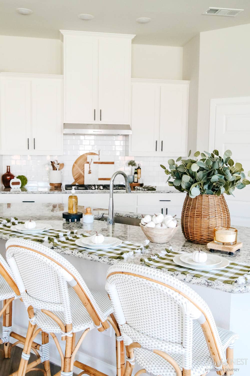 White kitchen with a basket used as a vase filled with eucalyptus leaves. View of the stove with cutting boards lined up.