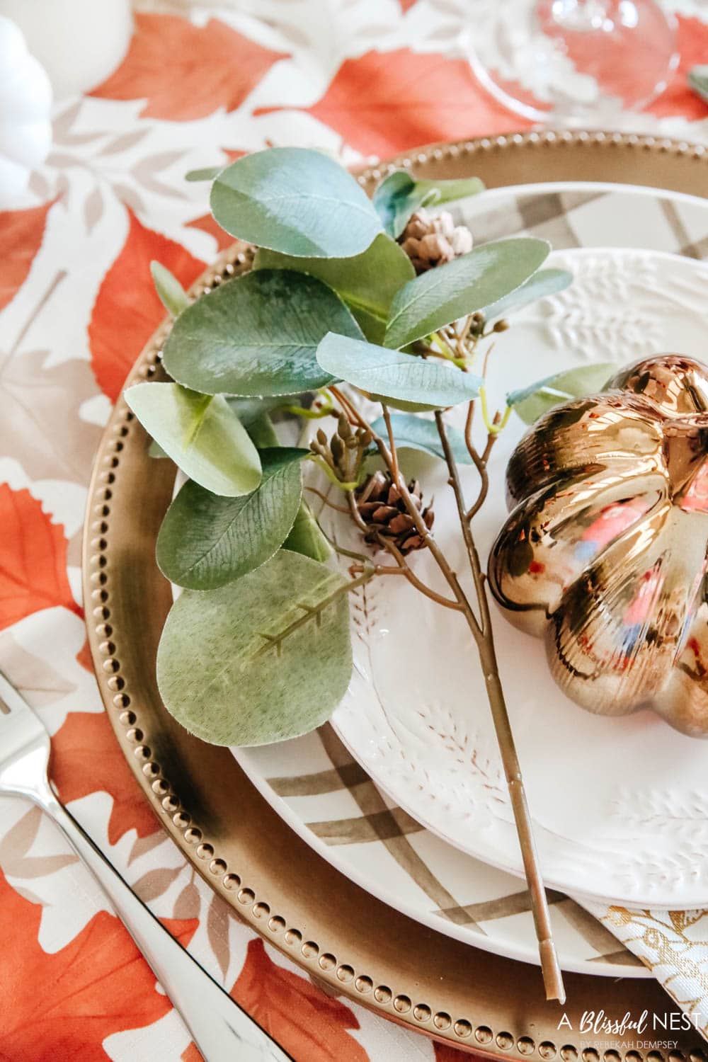 A faux eucalyptus stem on the side of the plate next to a bronze pumpkin