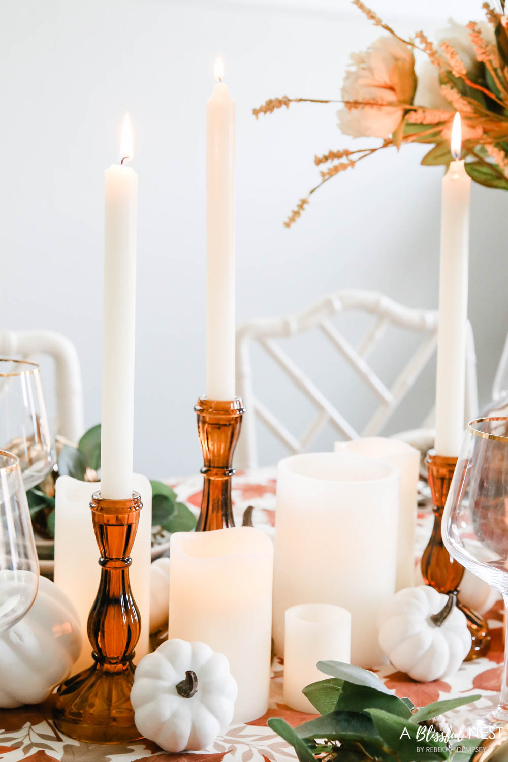 Amber colored tapered candle holders lit next to white pumpkins