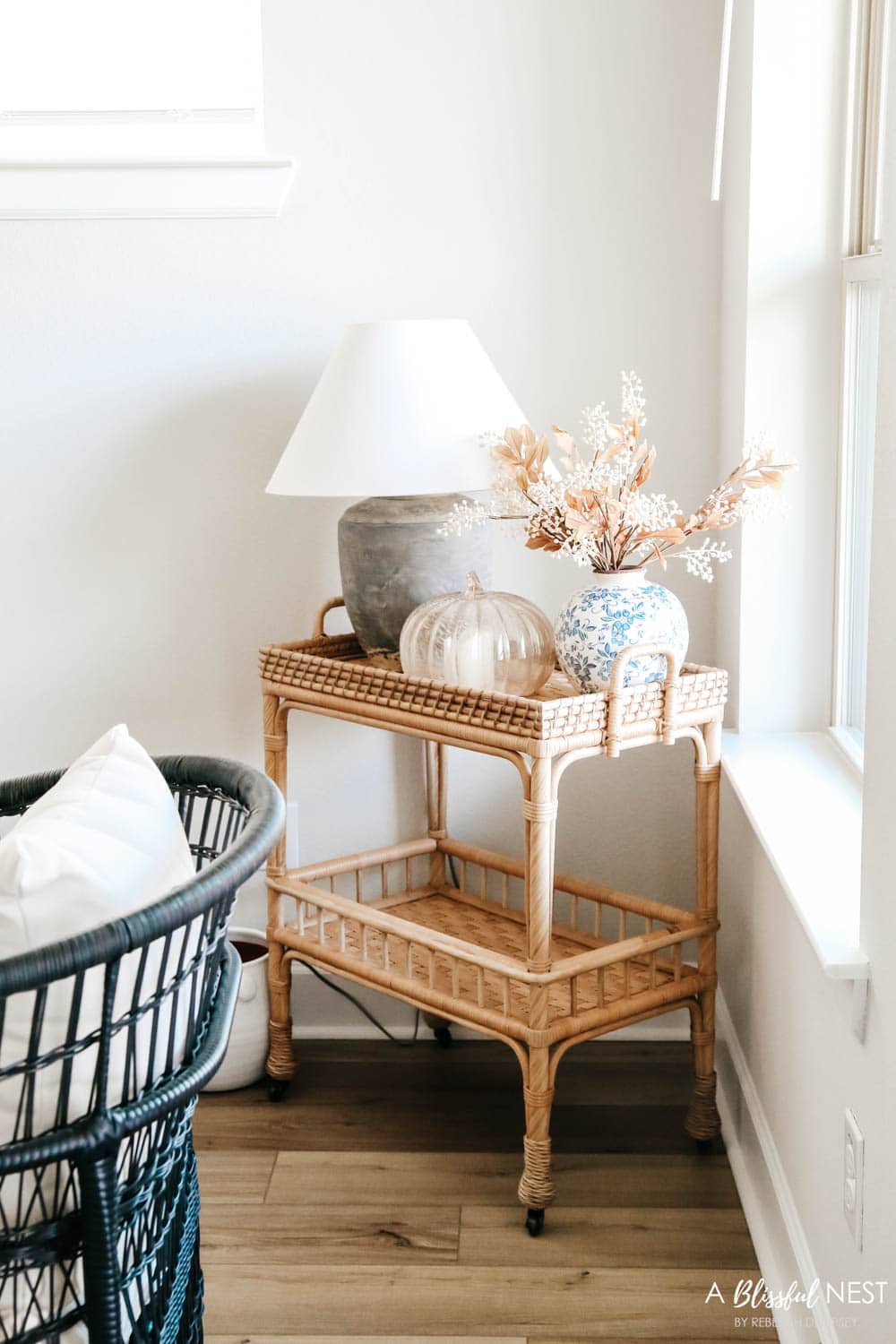 Rattan bar cart with grey table lamp and fall foliage with a glass pumpkin