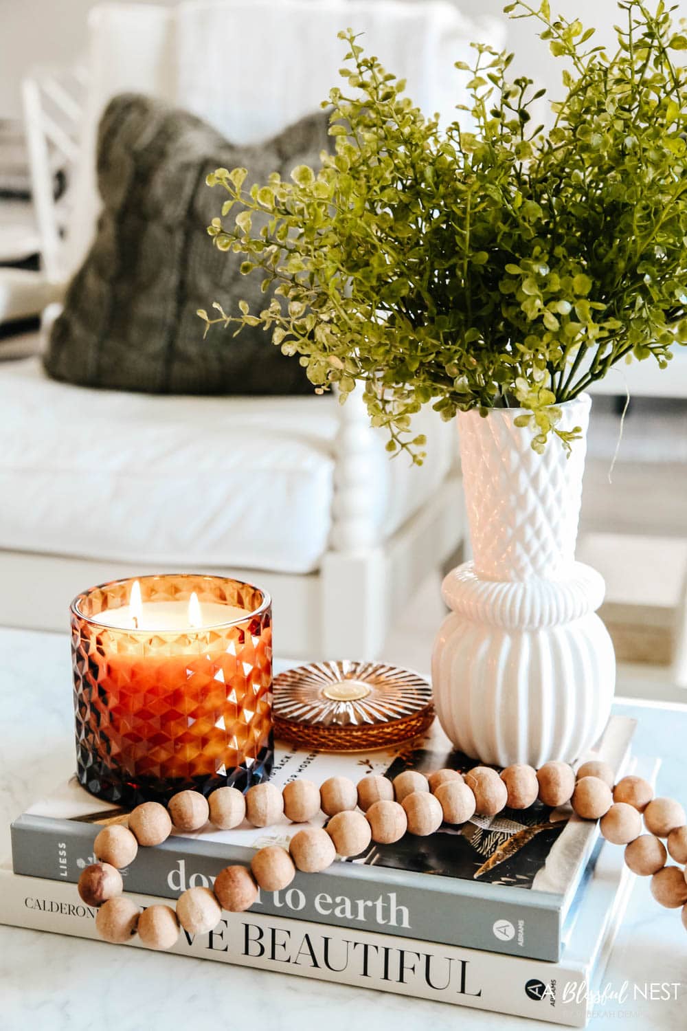 Amber colored candle next to a white vase with maidenhair in it on a coffee table