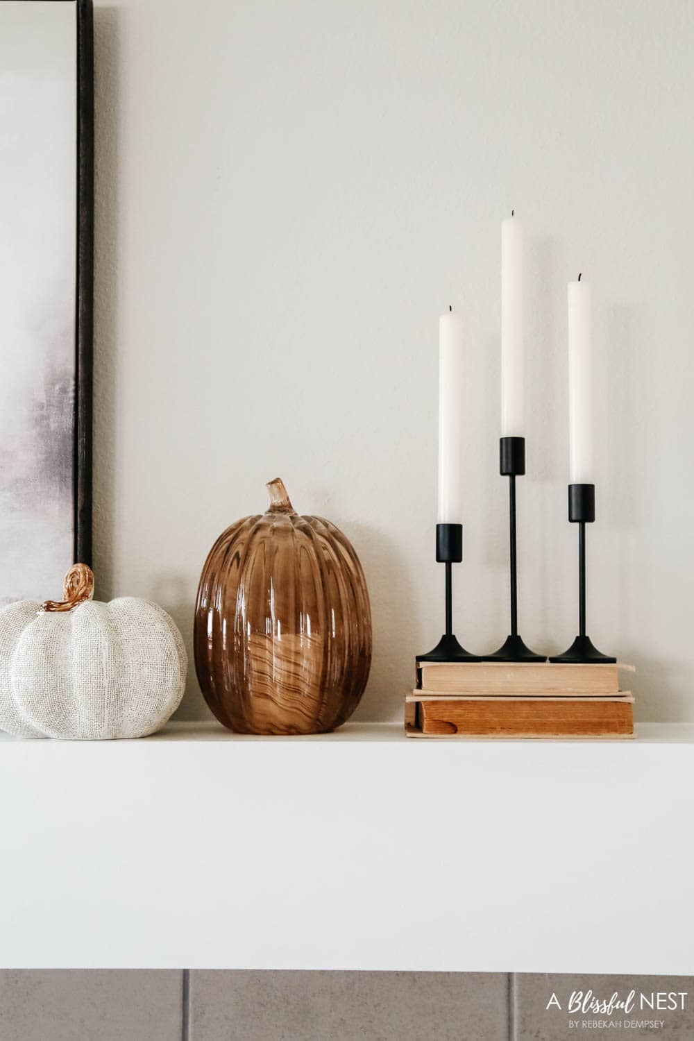 Cluster of black candlesticks on top of vintage books with pumpkins on top of a fireplace mantle