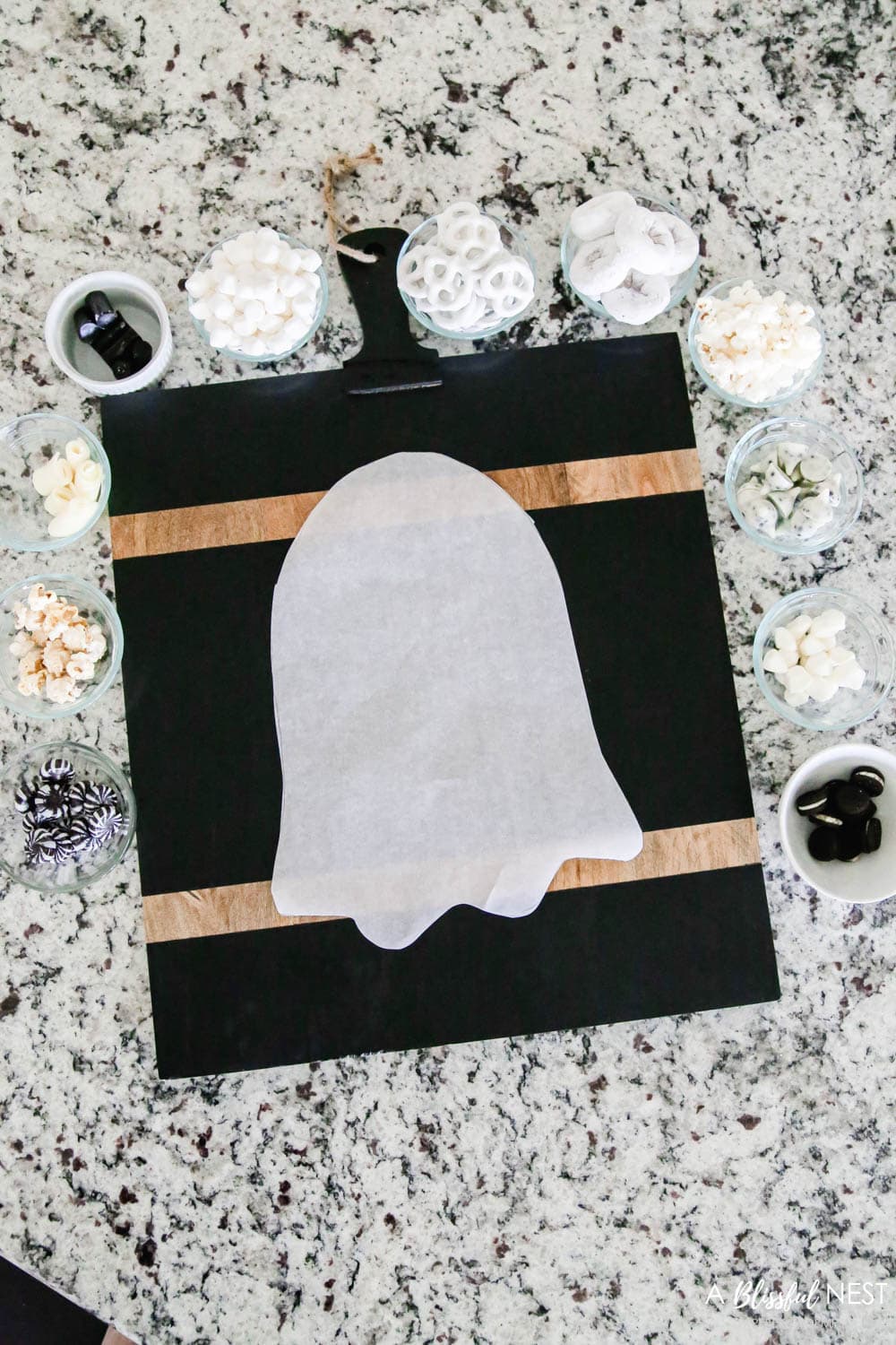 Cutting board with cut out ghost outline on parchment paper with candies in bowls
