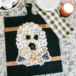 A black cutting board with sweet treats and cheeses laid out to look like a Halloween ghost.