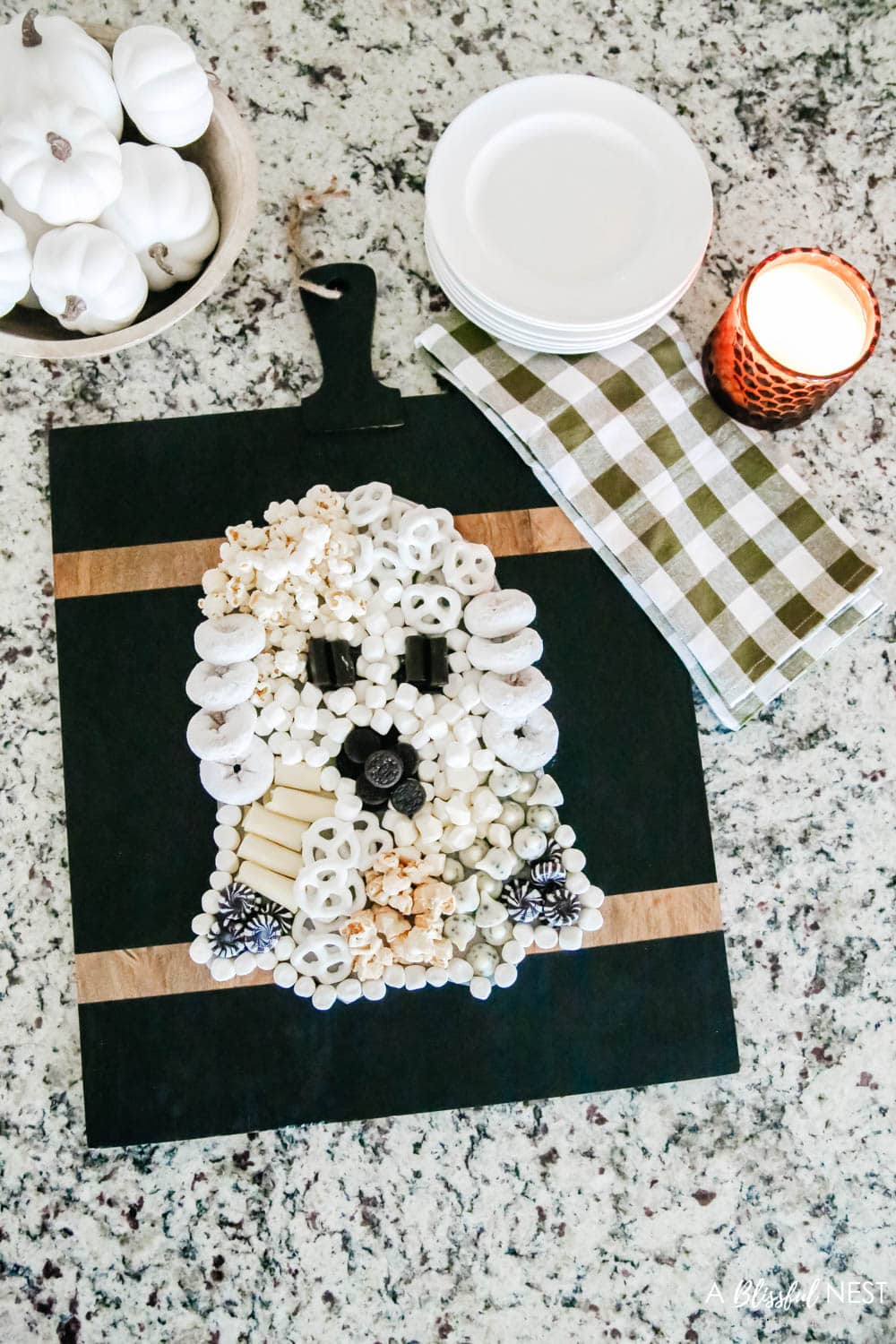 A black cutting board with sweet treats and cheeses laid out to look like a Halloween ghost.