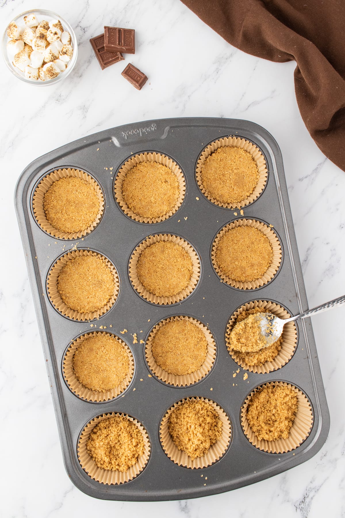 Cupcake pan with liners filled with graham cracker crust mixture packed down into the bottom.