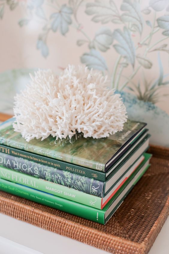 Stack of coffee table books in shades of green with coral sitting on top