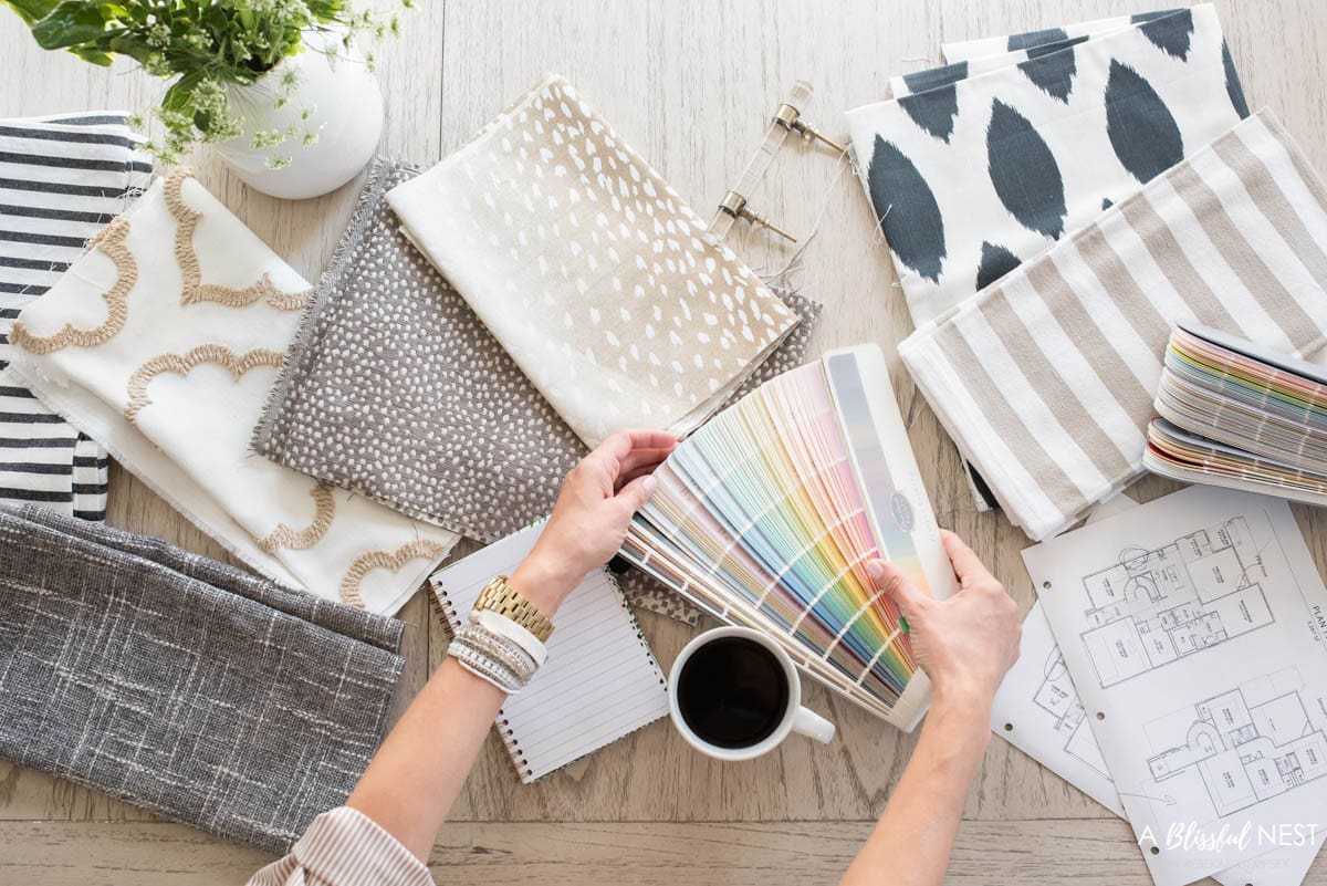 Neutral colored fabrics, paint decks, and building plans laid out on a table.