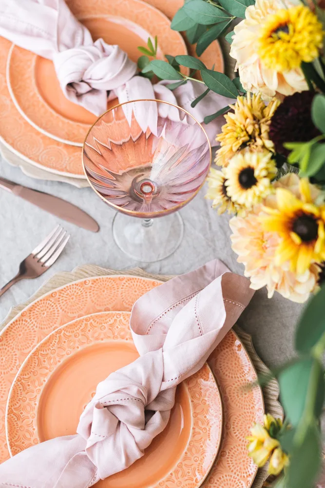 Layers of plates in a beautiful orange shade with a lilac cloth napkin tied on top.