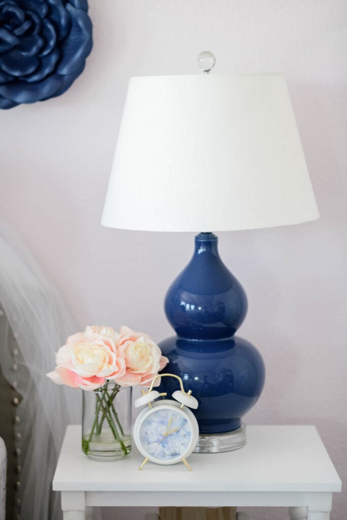 Navy blue table lamp on the white side table next to a bed