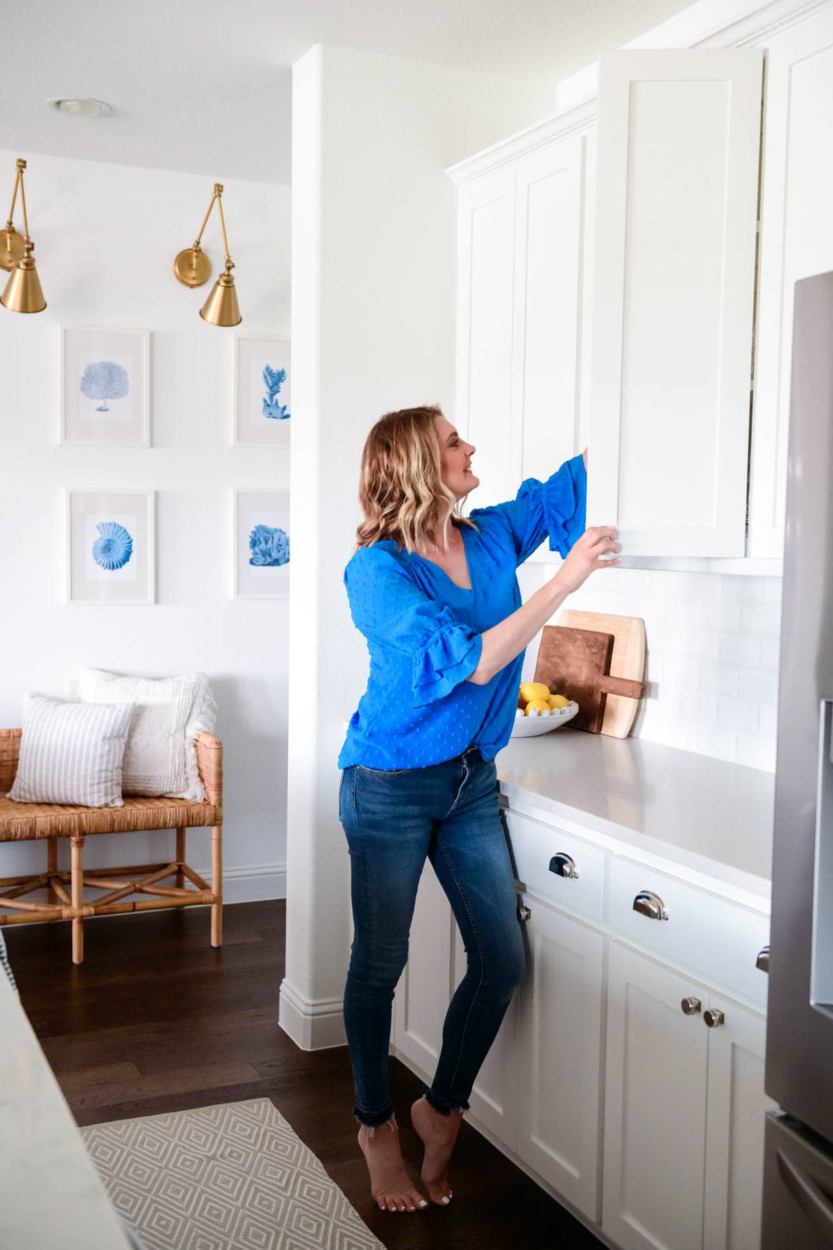 White kitchen with gold sconces for lighting. Pulling plates out of a cabinet.