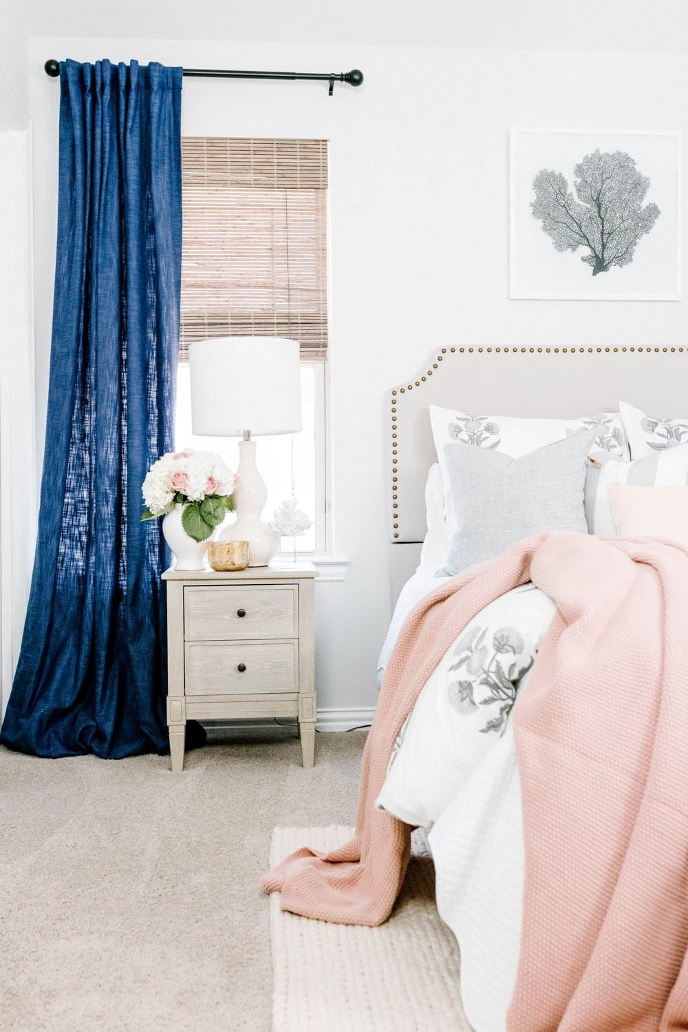 Bedroom with a grey headboard with nailheads and nay and white decor accents. 