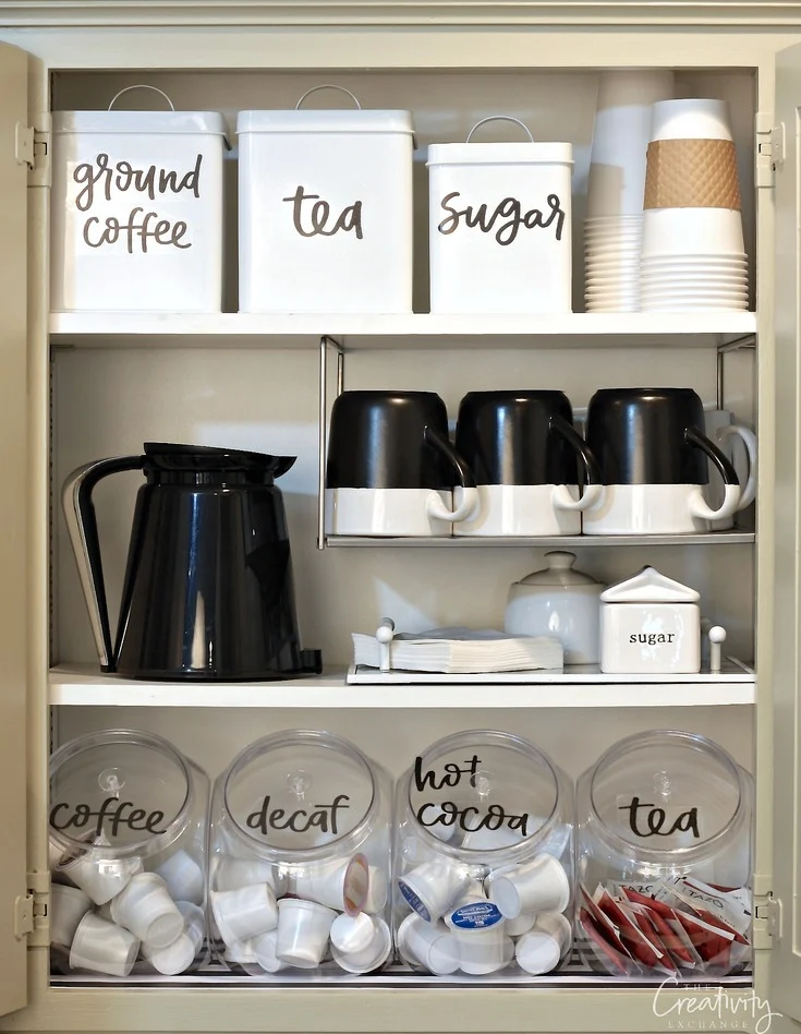 Inside a coffee cabinet with canisters filled with coffee pods, black kettle, coffee mugs