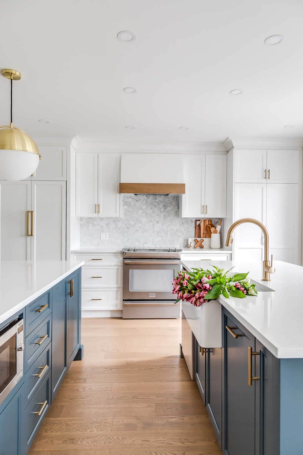 Grey blue kitchen cabinets with white quartz countertops. Pink tulips in sink. Marble herringbone tile for backsplash