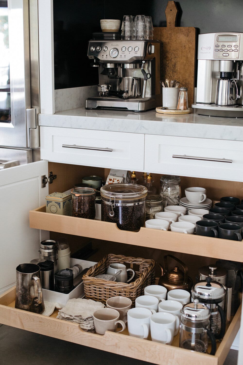 An at-home coffee station on a counter with pull out drawers below for storage.