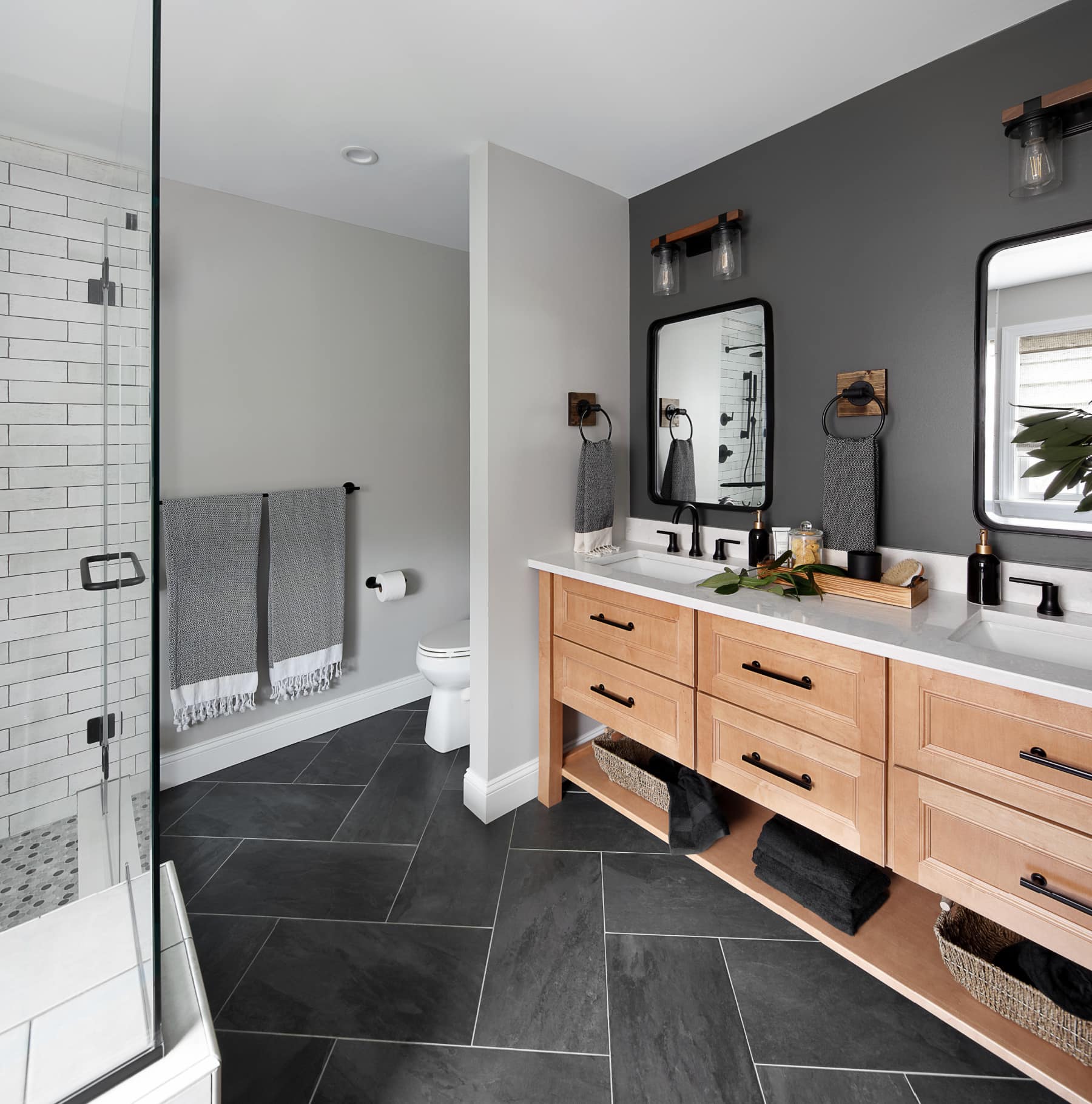 Dark grey accent wall behind sink cabinets. Honey okay cabinets with matte black hardware.